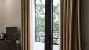 A room with a sliding glass door leading to a balcony, a dark wooden desk with a plant, and a kettle. - Aui Hotel (Hai Phong)