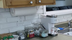Cuina amb armaris de fusta, taulell blanc i diversos electrodomèstics, incloent una cafetera.