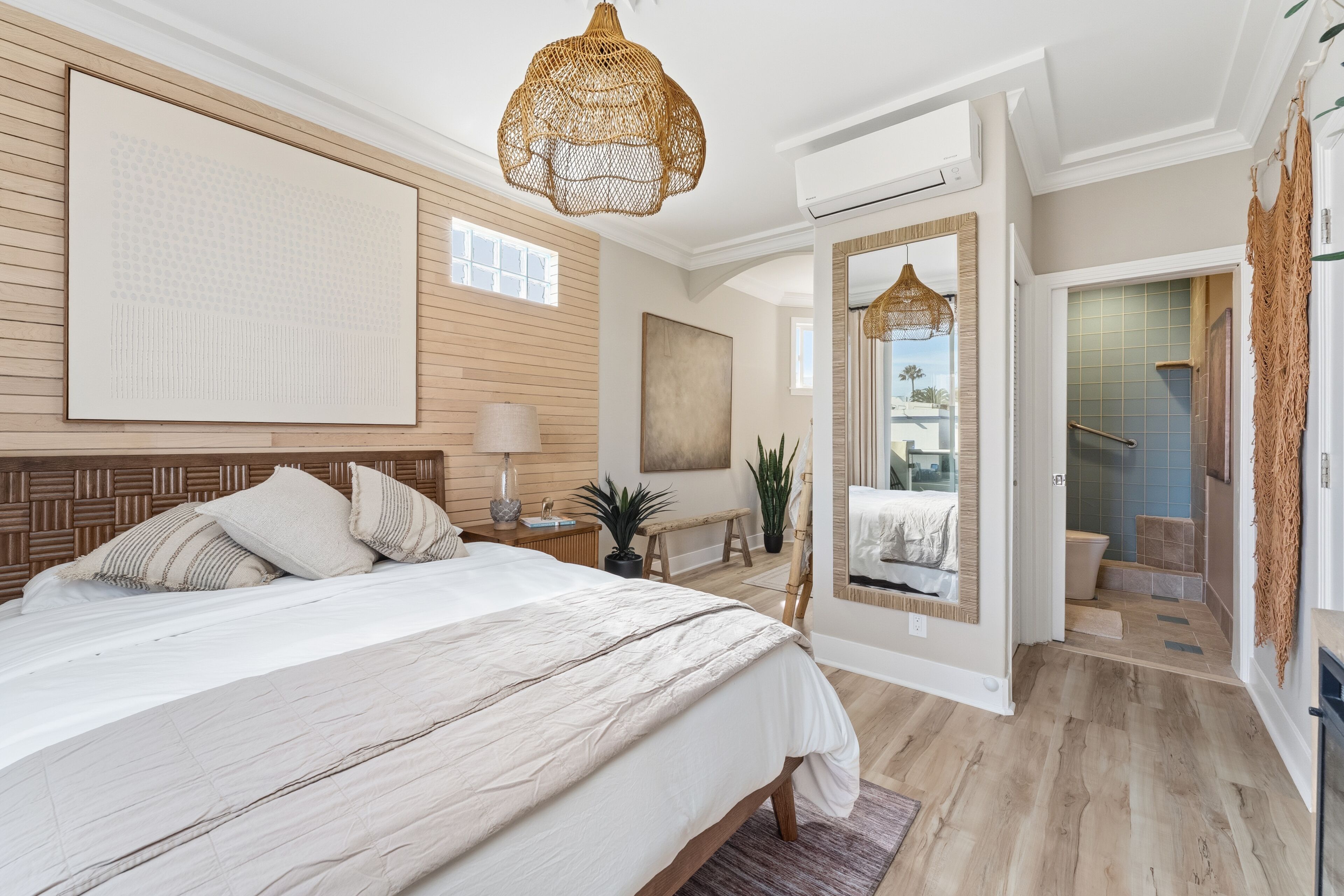 Een slaapkamer met een groot bed, een houten hoofdbord, een hanglamp, een grote spiegel en uitzicht op de badkamer.