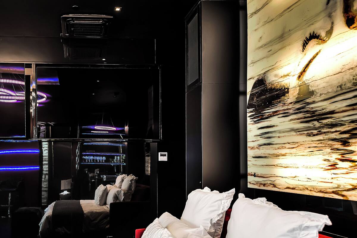 A modern hotel room with a large bed, a red accent wall, and a large abstract painting.