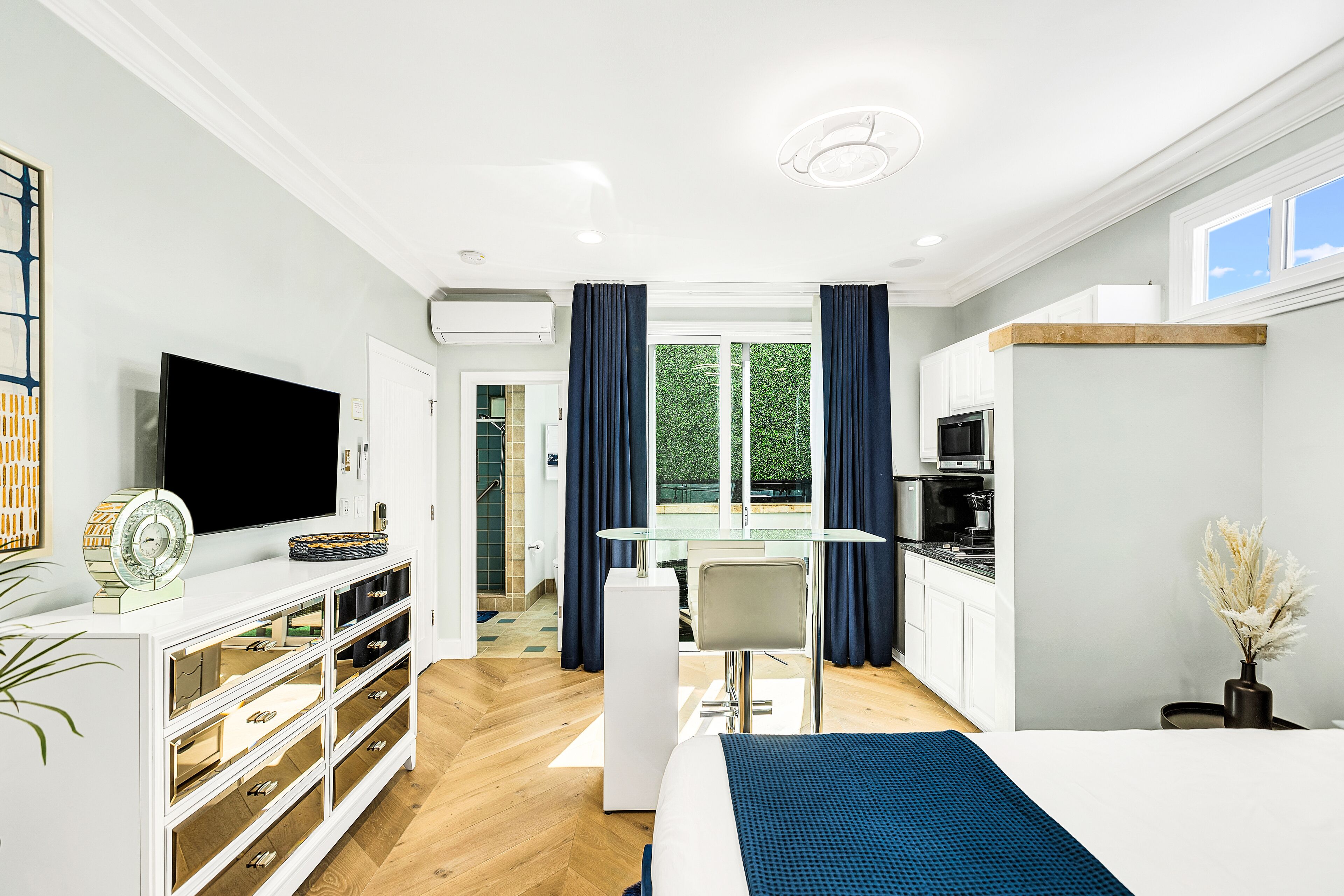 A modern hotel room with a large bed, a TV, a desk, and a view of the outdoors.