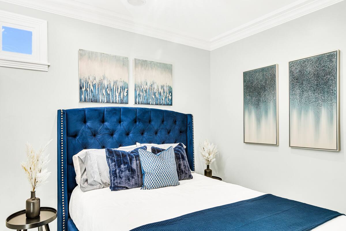 A bedroom with a large bed, a tufted headboard, and two wall-mounted paintings.
