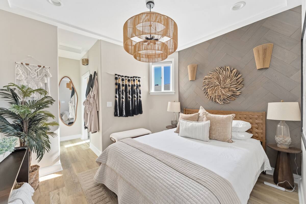A bedroom with a bed, bedside tables, a hanging light fixture, a window, and a plant.