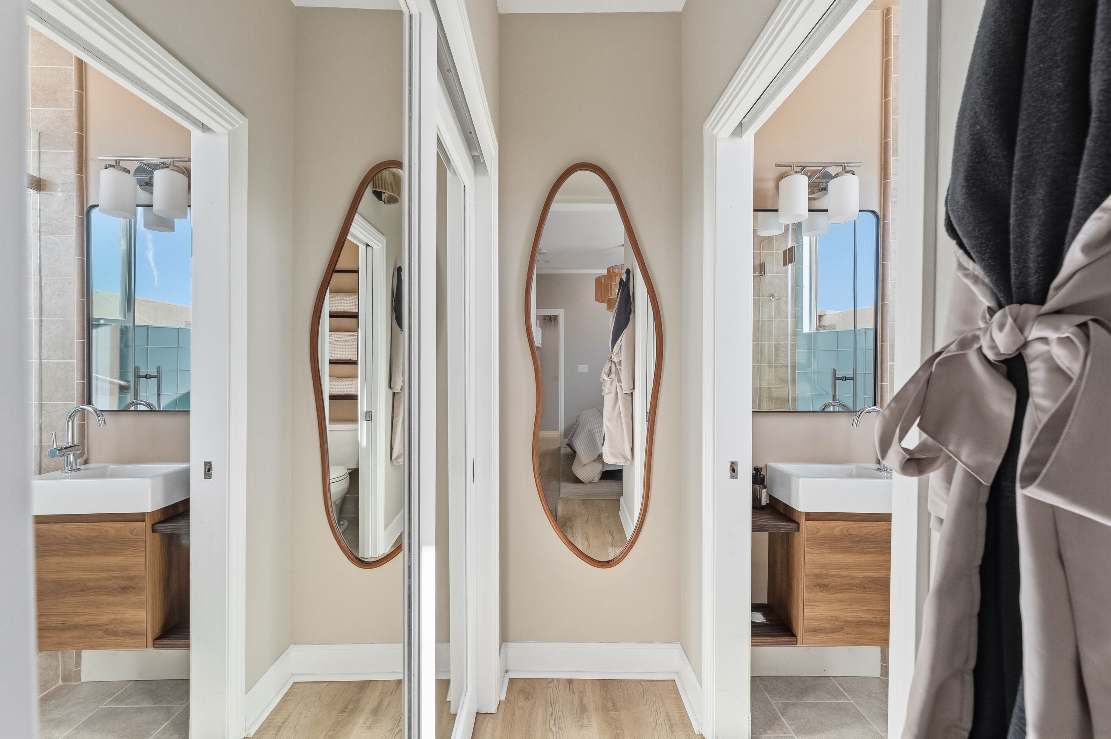 A hallway with mirrors, a sink, and a robe hanging on the right.