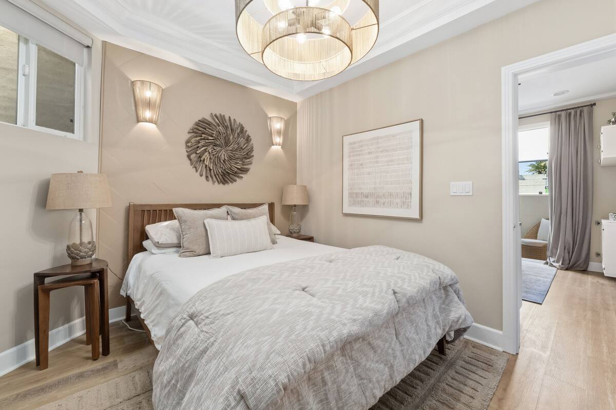 A bedroom with a large bed, two bedside lamps, a wall-mounted light fixture, and a door leading to another room.