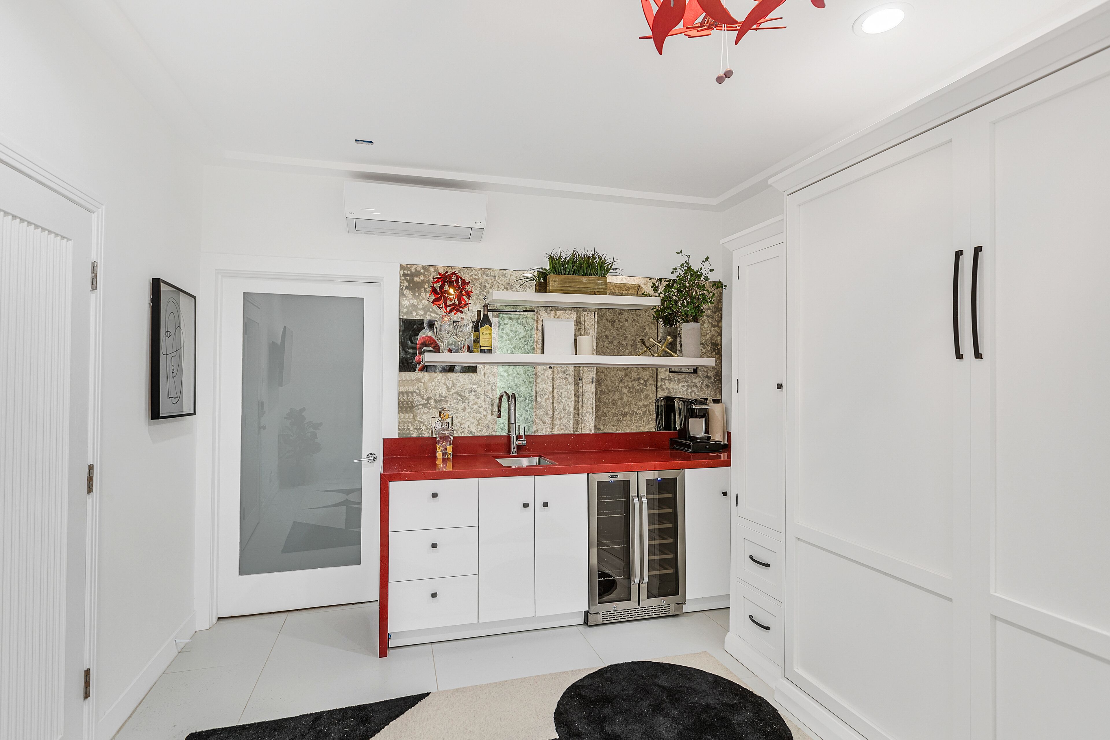 Una cocina moderna con armarios blancos, una encimera roja y un refrigerador para vinos empotrado.