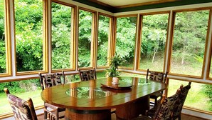 Un espace repas avec une table ronde en bois entourée de chaises, de grandes fenêtres et un ventilateur de plafond.