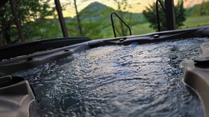 Scheibenwischer in Bewegung, Wasser spritzt auf die Scheibe, verschwommene Aussicht auf eine bewaldete Landschaft im Hintergrund.