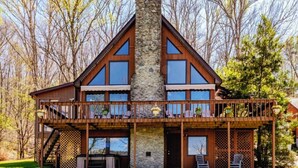 Une cabane à deux étages avec une cheminée en pierre, des balcons en bois et une terrasse dotée de meubles d’extérieur.