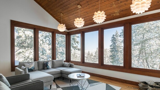 Ein modernes Wohnzimmer mit einer Eckcouch, einem Couchtisch und großen Fenstern mit Blick auf schneebedeckte Bäume.