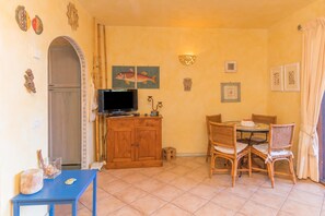 Un coin repas avec une table et des chaises, un téléviseur posé sur un meuble en bois, et des éléments de décoration murale comprenant des tableaux de poissons et un luminaire fixé au mur.