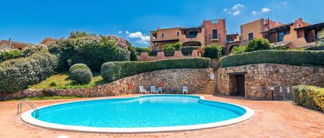 A swimming pool with a stone wall, a stone staircase, and a view of buildings in the background.