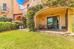 A courtyard with a table and chairs, a stone wall, and a building with a balcony. - Il Poggio A3 With Shared Pool, Porto San Paolo, Italy (Porto San Paolo)