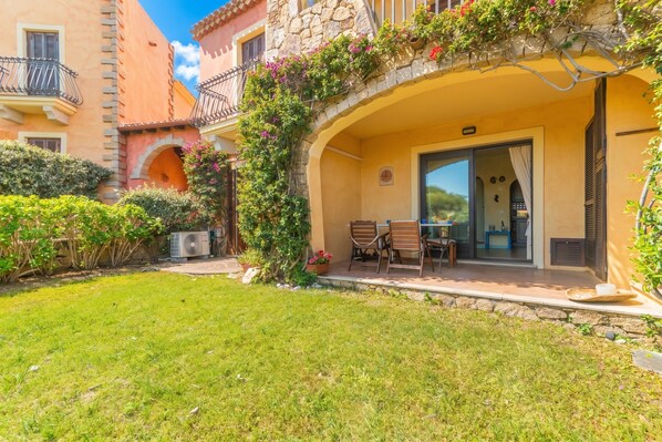 Une cour avec une table et des chaises, un mur en pierre et un bâtiment doté d’un balcon.