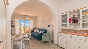 A cozy living area with a dining table, chairs, a sofa, and a kitchen with cabinets and shelves.