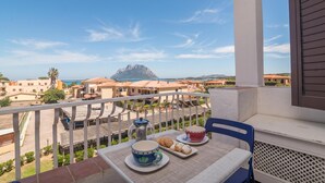 A balcony with a table set for tea, a view of buildings and a mountain, and a clear sky.