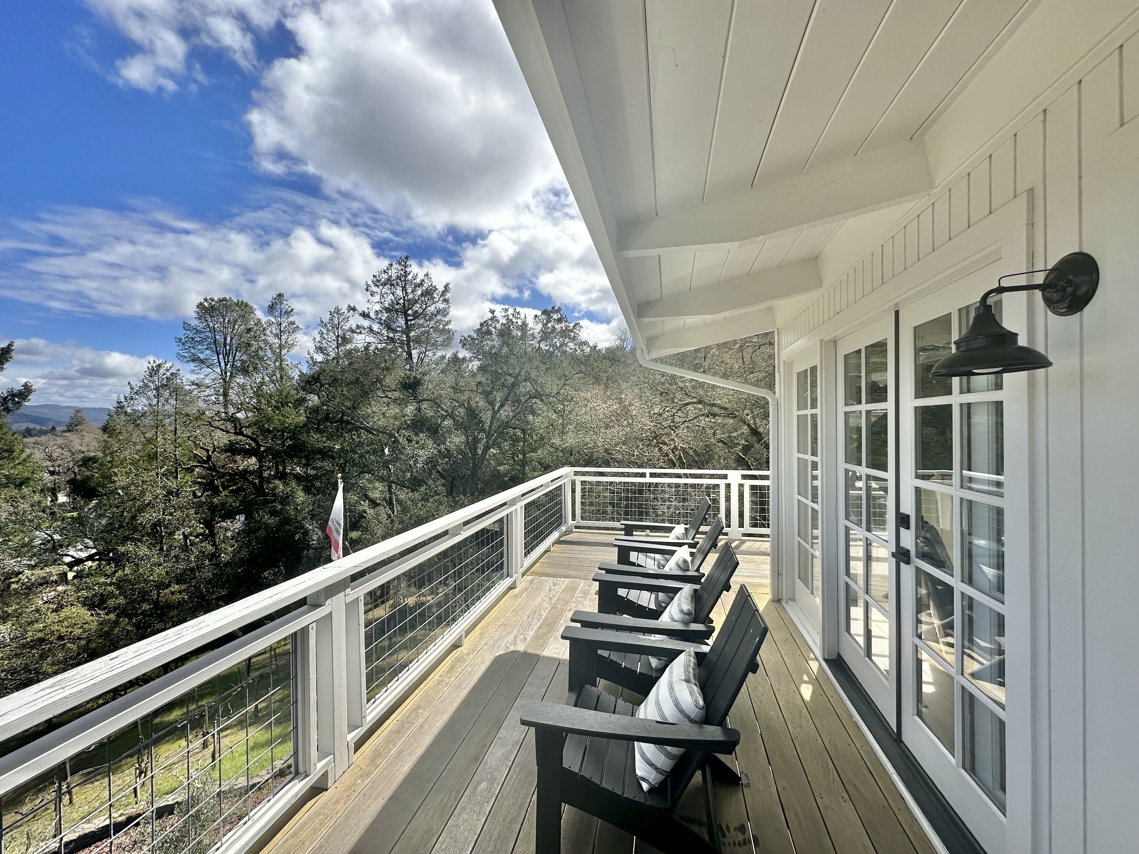 A wooden deck with outdoor seating, a railing, and a view of trees and mountains.