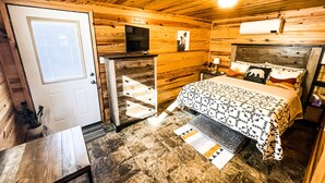A wooden cabin-style room with a bed, a television, and a door.
