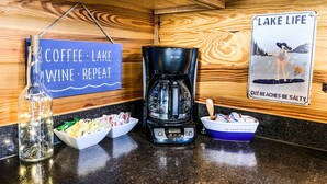 A kitchen counter with a coffee maker, a sign reading "Coffee, Lake, Wine, Repeat", and a sign with a woman paddleboarding.