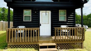 A log cabin with a porch, two windows, and a door.