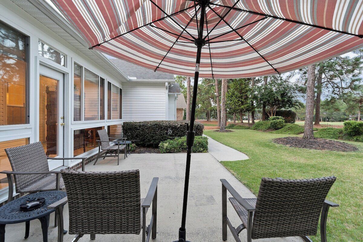 Een terras buiten met rieten stoelen en een gestreepte parasol.