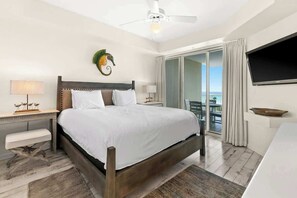 A hotel room with a bed, a nightstand, a desk, a chair, a television, and a balcony with a view.