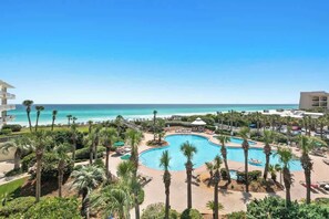 A resort with a large central pool, palm trees, and a view of the ocean.
