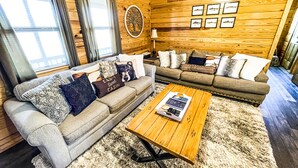 A cozy cabin interior with two sofas, a coffee table, and a wooden wall with framed pictures. - Cabin #3 • 1 Mile to DeGray Lake (Bismarck)