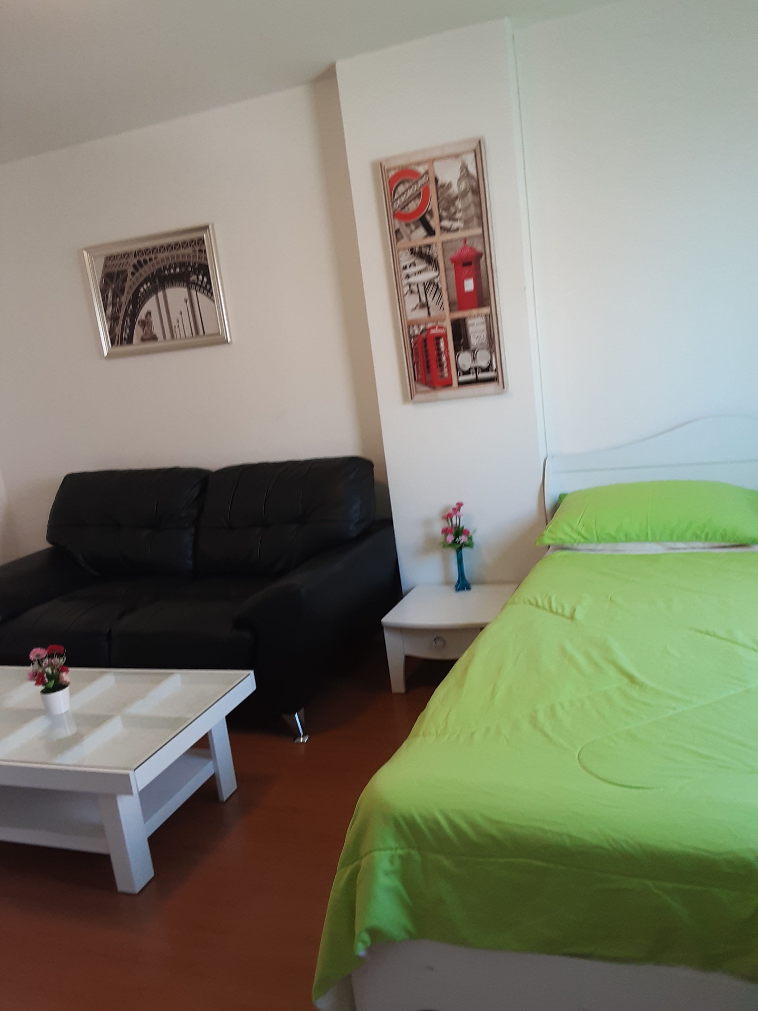 A room with a bed, a sofa, a small table with a vase of flowers, and two framed pictures on the wall.