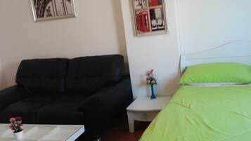 A room with a bed, a sofa, a small table with a vase of flowers, and two framed pictures on the wall.
