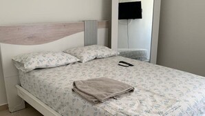 Una cama bien hecha con una colcha y almohadas estampadas con motivos florales, una mesita de noche con un control remoto y un espejo en la pared.