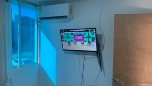 Habitación con televisión instalada mostrando un evento deportivo, aire acondicionado y ventana con cortinas.