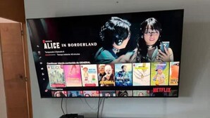Un televisor montado en la pared con el logotipo de Netflix, un armario blanco debajo y una puerta a la izquierda.