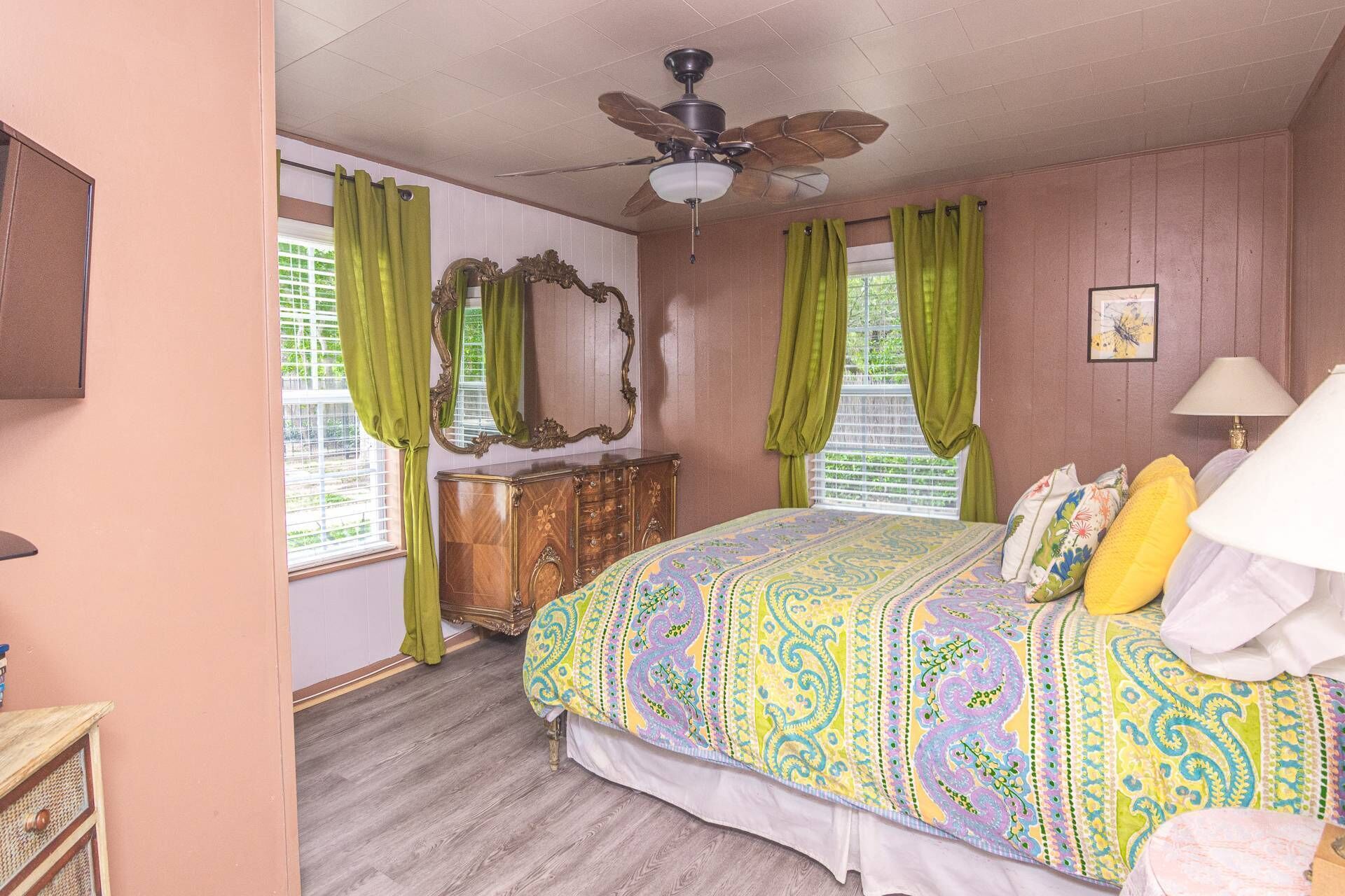 A bedroom with a bed, a dresser, a ceiling fan, and green curtains.
