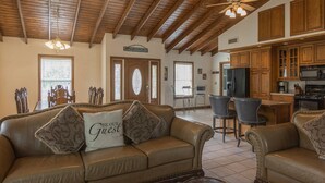 A spacious living room with a leather sofa, a dining area with chairs, wooden cabinets, and a kitchen area with appliances.