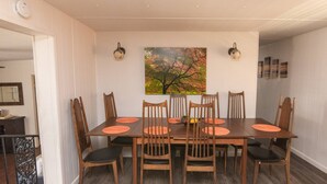 A dining room with a wooden table and six chairs, a painting of a tree on the wall, and a light fixture above the table. - Casa del Lago! Lakefront Retreat with Semi-Private Cove, Deck, and Firepit - Ideal for R&R! (Laguna Park)