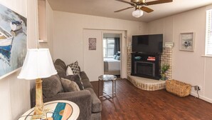 A living room with a fireplace, a ceiling fan, and a television. - Casa del Lago! Lakefront Retreat with Semi-Private Cove, Deck, and Firepit - Ideal for R&R! (Laguna Park)