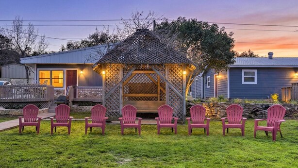 A gazebo with a lattice roof and wooden walls, surrounded by six Adirondack chairs in a grassy area. - Casa del Lago! Lakefront Retreat with Semi-Private Cove, Deck, and Firepit - Ideal for R&R! (Laguna Park)