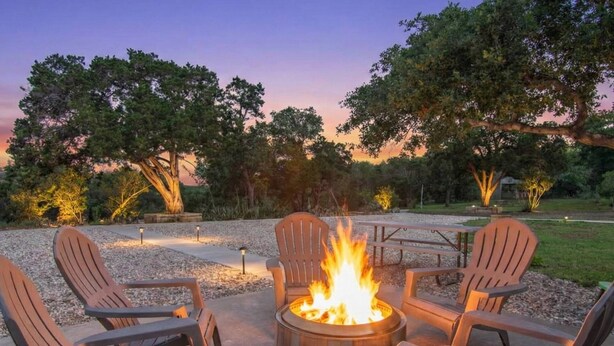 A fire pit with chairs around it, set in a gravel area with trees in the background.