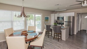 A modern kitchen with a central island, white cabinets, stainless steel appliances, and a dining area with a round table and chairs.