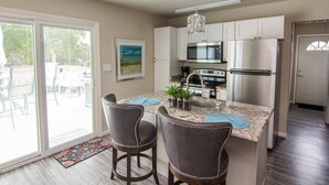 A kitchen with a central island, two bar stools, stainless steel appliances, and a dining area with a view.