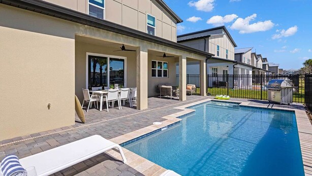 A swimming pool with lounge chairs and a patio area, surrounded by a fence and a building with large windows. - Hi255sd: 6 Bed, Enchanted House, Casino (Melbourne Beach)