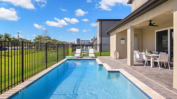A rectangular swimming pool with a tiled deck, surrounded by a black metal fence. There are lounge chairs and a table with chairs on the deck. - Hi280sd: 5 Bed, Under The Sea, Gameroom (Melbourne Beach)
