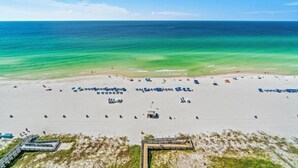 An aerial view of a beach with clear turquoise waters, a sandy shore, and several beach umbrellas and lounge chairs. - Gulfcrest 19th-Floor | Beachfront | Huge Balcony (Panama City Beach)