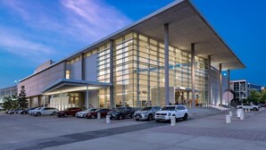 A modern building with a large glass facade, a flat roof, and a parking lot with several cars. - 3 Spacious Suites with Fully-equipped Kitchens! Pool Access & Sports Court! (Richardson)
