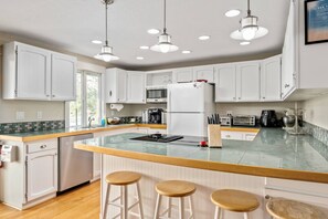 Enjoy cooking in this well-equipped kitchen with a central island, white cabinetry, and a large window offering a view of the outdoors.