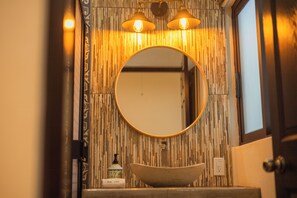 A bathroom with a round mirror, a vessel sink, and a wall-mounted light fixture.