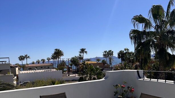A rooftop terrace with a glass table and chairs, overlooking a coastal area with palm trees and mountains. - At the best location and ocean view (Loreto)