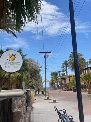 A sign for 'Las Victorias' in Loreto, Mexico, with a paved walkway, palm trees, and a building in the background.