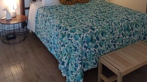 A bedroom with a wooden headboard, floral bedspread, two decorative pillows, a bedside table with a lamp, and a small wooden bench. - At the best location and ocean view (Loreto)